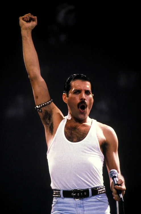Freddie Mercury, photographed during a concert, wearing a white T-shirt and jeans.