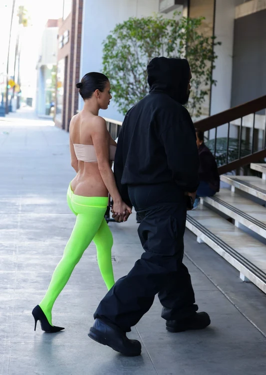 Bianca Censori holds hands with Kanye West. She is wearing green tights and a beige bustier.